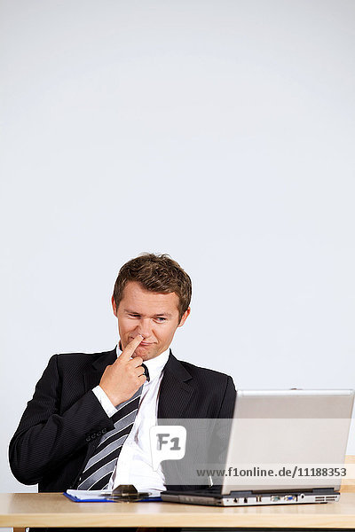 Businessman picking nose  looking at laptop in office
