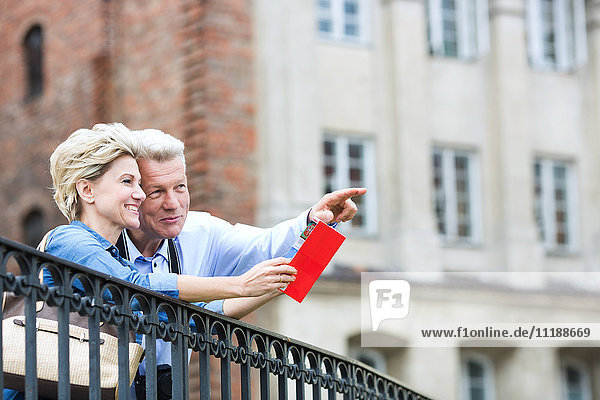 Smiling middle-aged man showing something to woman with guidebook in city