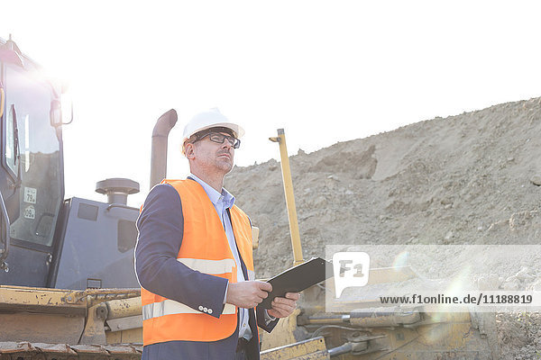 Engineer looking away while holding clipboard at construction site
