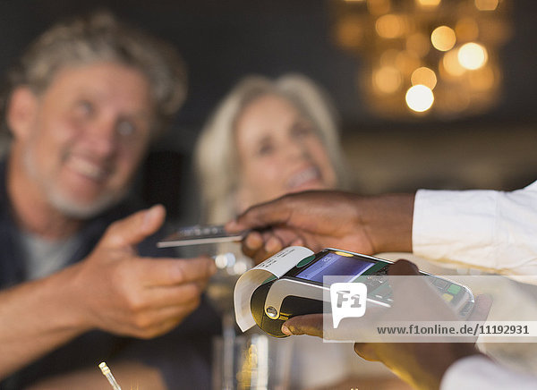 Close up waiter using credit card machine returning credit card to couple