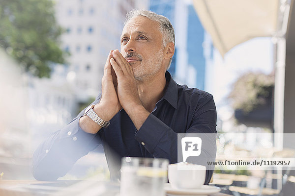Pensive man drinking coffee at urban sidewalk cafe