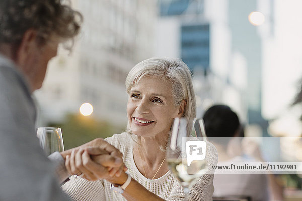 Zärtliches älteres Paar hält sich an den Händen und trinkt Weißwein in einem städtischen Straßencafé