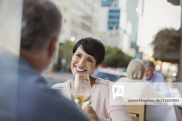 Smiling couple toasting white wine glasses at urban sidewalk cafe