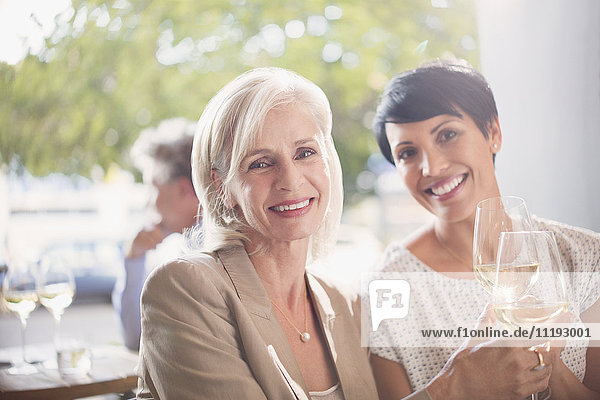 Portrait lächelnde Mutter und Tochter stoßen mit Weißweingläsern in einem sonnigen Restaurant an