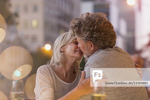 Affectionate senior couple kissing at urban sidewalk cafe
