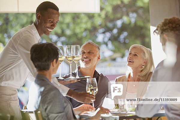 Waiter serving white wine to couples at restaurant table