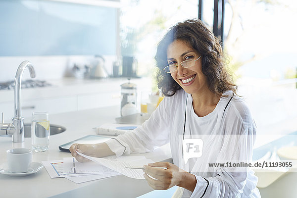 Porträt einer lächelnden Geschäftsfrau im Bademantel  die in der Küche Papierkram durchgeht