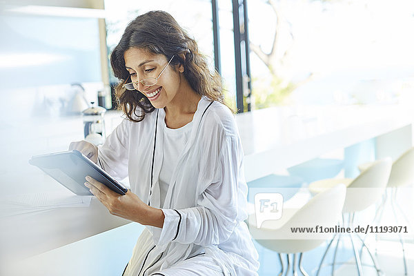 Lächelnde Geschäftsfrau im Bademantel bei der Arbeit mit einem digitalen Tablet in der Küche