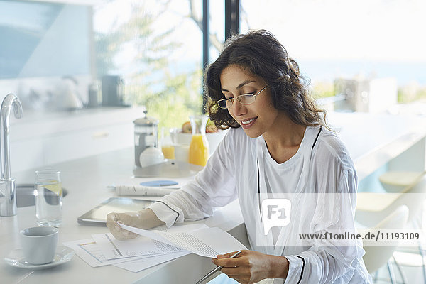 Geschäftsfrau im Bademantel bei der Durchsicht von Papierkram am Küchentisch