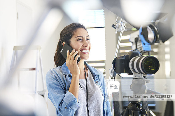 Lächelnde Fotografin  die hinter der Kamera im Studio mit einem Handy spricht