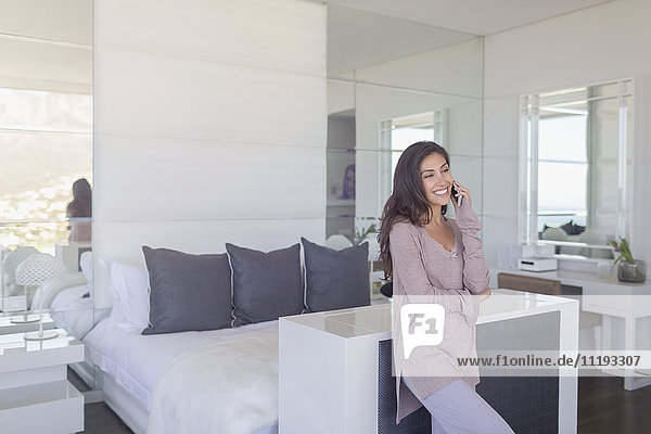 Smiling woman talking on cell phone in luxury modern bedroom