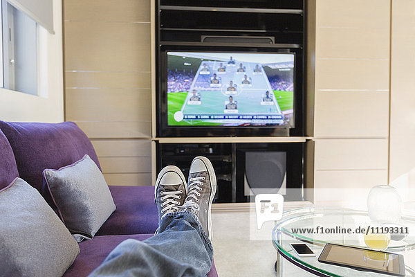 Persönliche Perspektive Mann mit Füßen oben beobachten Fußballspiel im Fernsehen im Wohnzimmer