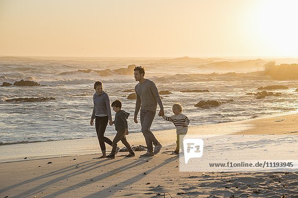 Happy young family walking on the beach at sunset