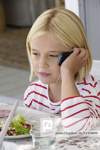 Kleines Mädchen  das beim Essen am Handy spricht