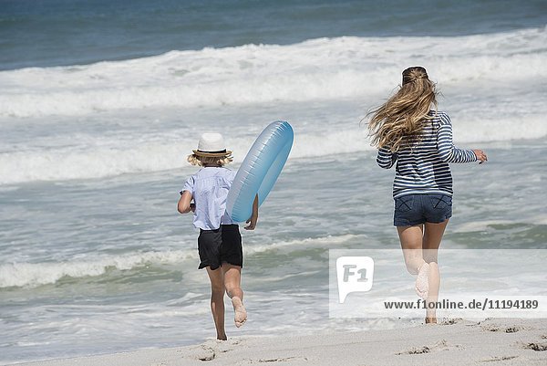 Rückansicht einer Frau  die mit ihrer Tochter am Strand läuft.