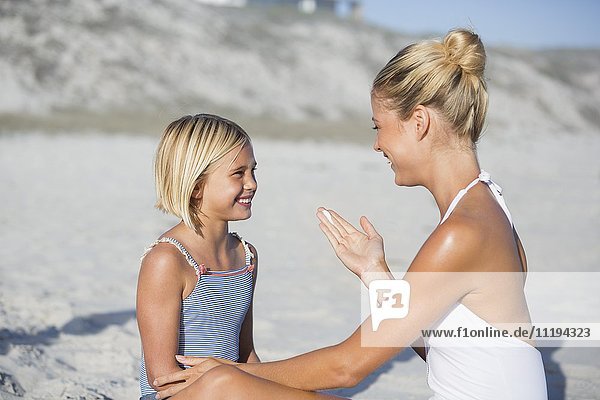 Mutter und Tochter lächeln sich am Strand an.