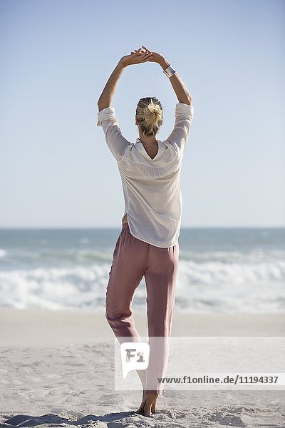 Schöne junge Frau beim Yoga am sonnigen Strand