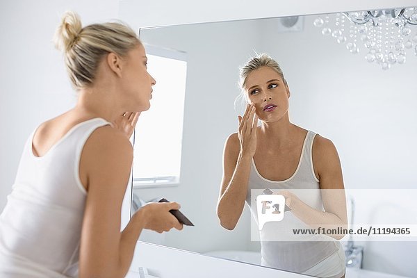 Schöne junge Frau  die Feuchtigkeitscreme auf ihr Gesicht im Badezimmer aufträgt.