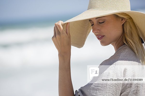 Schöne junge Frau mit Sonnenhut am Strand