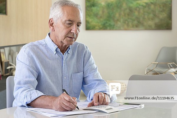 Senior man using a calculator while doing paperwork at home