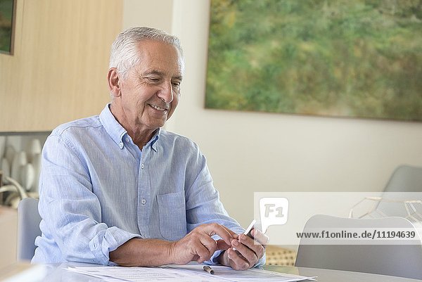 Happy senior man using a phone while doing paperwork at home