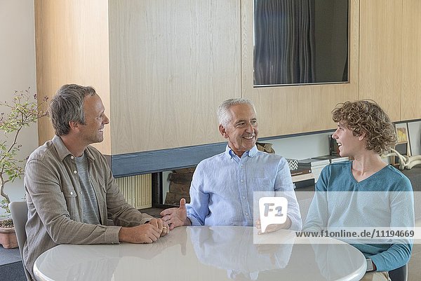 Glücklicher Senior im Gespräch mit Sohn und Enkel im Wohnzimmer