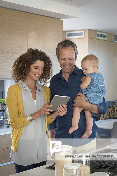 Paar mit digitalem Tablett mit ihrer Tochter in der Küche