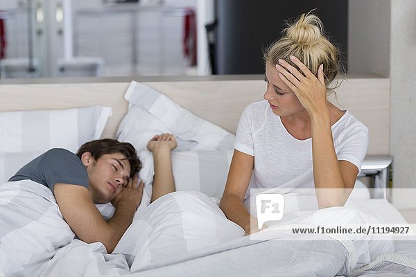 Junge Frau schaut ihren Mann an  der auf dem Bett schläft
