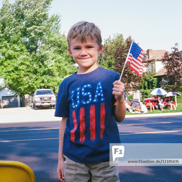Junger Junge trägt ein USA-T-Shirt und winkt mit der amerikanischen Flagge