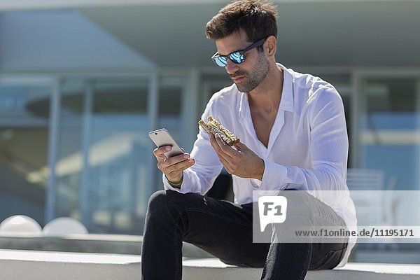 Mid Erwachsene Mann mit einem Smartphone und essen Sandwich