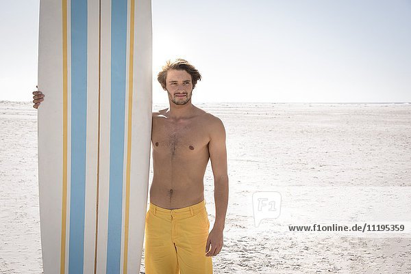 Glücklicher junger Mann mit Surfbrett am Strand
