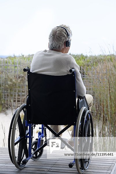 Älterer Mann im Rollstuhl  der Musik über Kopfhörer im Freien hört.