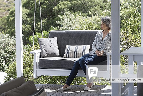 Fröhliche Frau entspannt sich auf dem Schaukelstuhl auf der Veranda