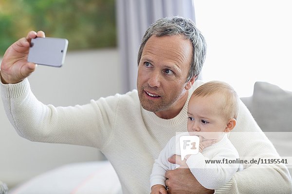 Glücklicher Vater mit seiner kleinen Tochter  die Selfie mit Fotohandy nimmt.