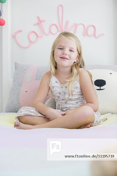 Porträt eines glücklichen kleinen Mädchens  das auf dem Bett sitzt