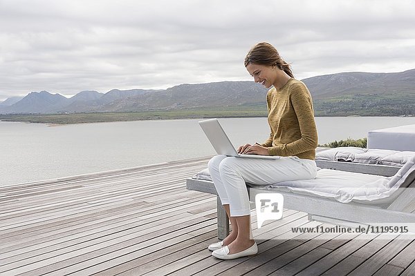 Glückliche schöne Frau mit einem Laptop am Seeufer