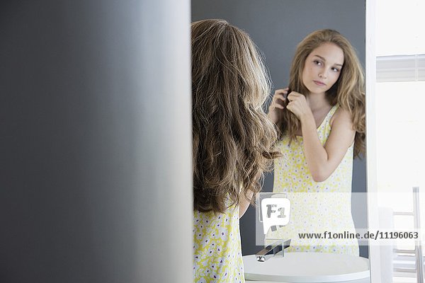 Teenage girl examining her hair in mirror
