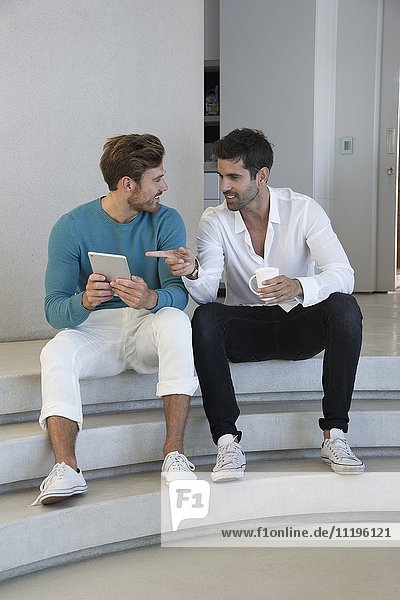 Happy male friends using a digital tablet at home