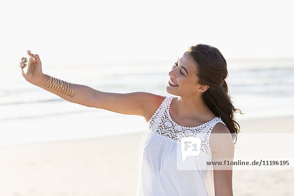 Fröhliche junge Frau nimmt Selfie mit Smartphone am Strand
