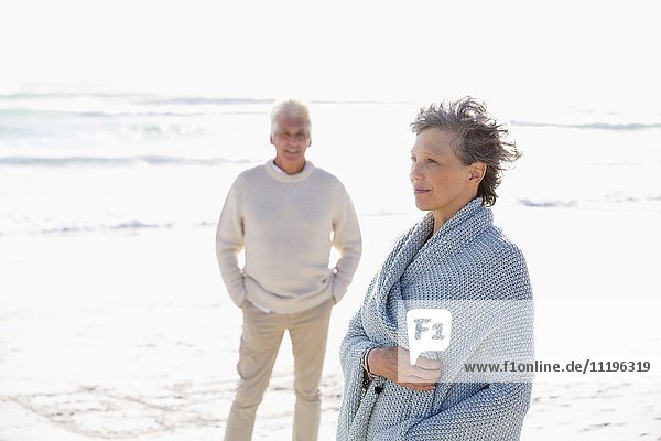 Frau am Strand stehend mit ihrem Mann im Hintergrund