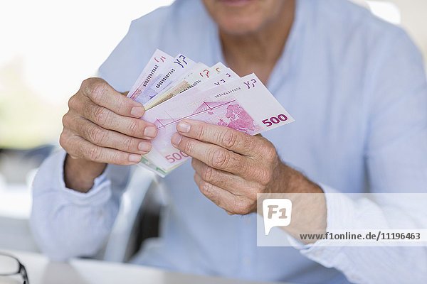 Mittelteilansicht eines älteren Mannes beim Zählen von Geldscheinen