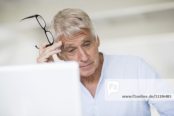 Besorgter älterer Mann Kopf in Hand mit Laptop auf dem Tisch