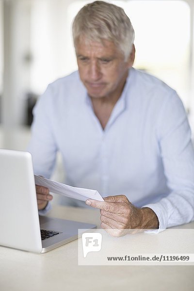 Senior man reading a letter with laptop on table
