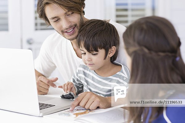 Vater lehrt die Kinder über die Weltkarte  während sie den Laptop zu Hause benutzen.