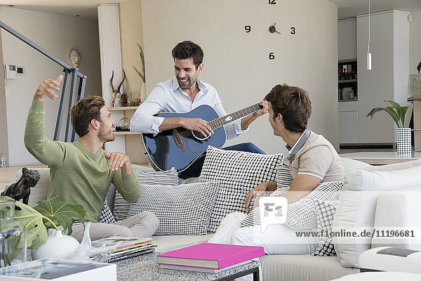 Glücklicher Mann spielt Gitarre mit seinen Freunden in seiner Nähe.