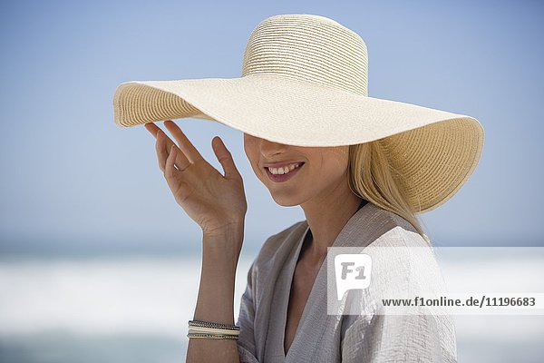 Glückliche junge Frau mit Sonnenhut am Strand