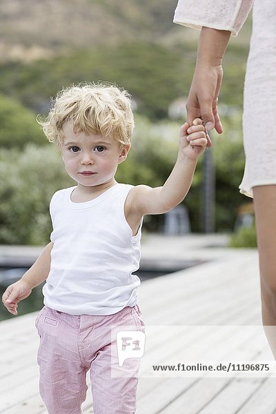 Porträt eines kleinen Jungen  der mit seiner Mutter am Pool spazieren geht.