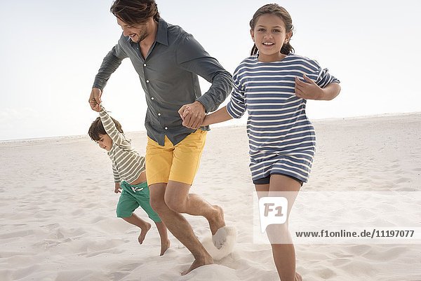 Glücklicher Vater läuft mit seinen Kindern am Strand.