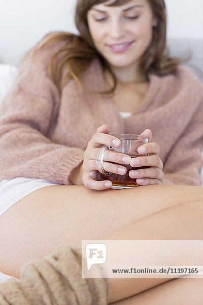 Glückliche Frau mit Tasse Kräutertee im Bett