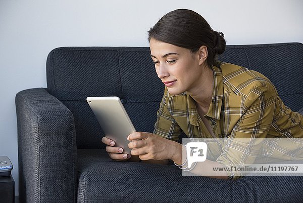 Junge schöne Frau mit einem digitalen Tablett auf der Couch